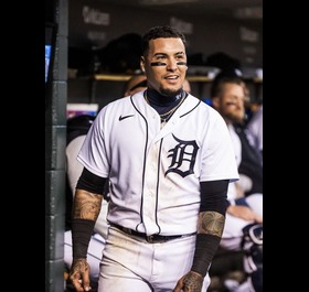 Detroit baseball player in a white uniform walking through the dugout with teammates out of focus